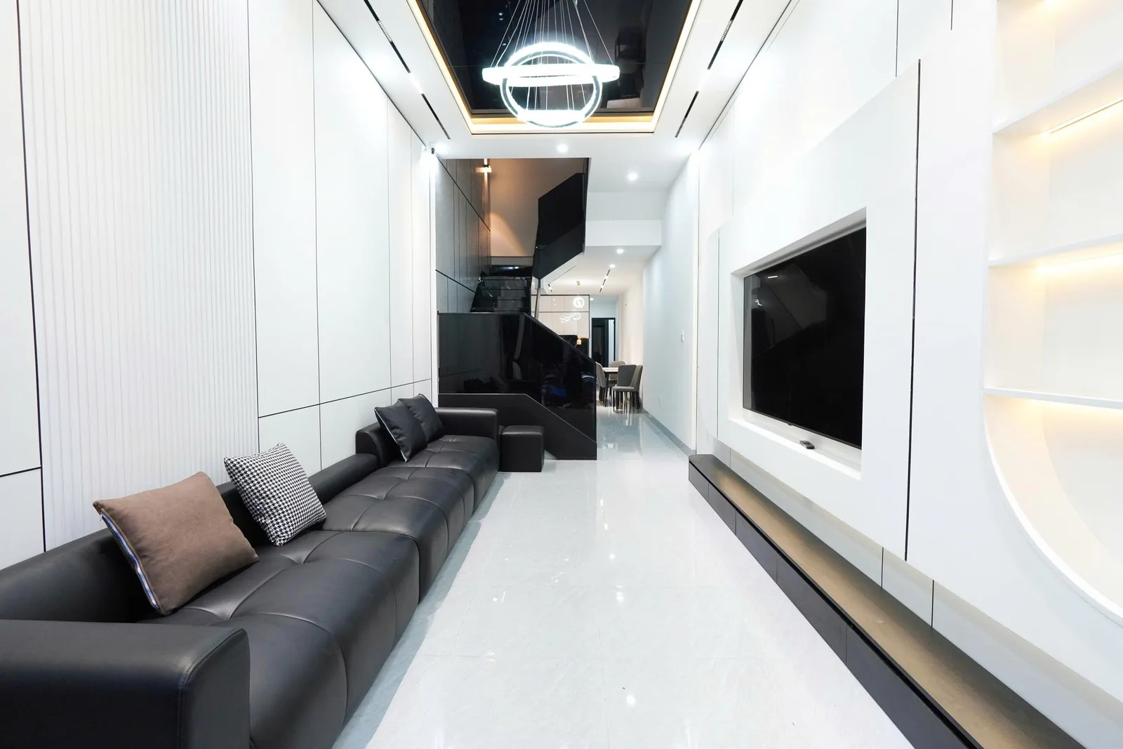 Phòng khách nhà phố Phú Tài, Quy Nhơn: sofa da đen dài và hệ tủ trắng chạy dọc thân nhà